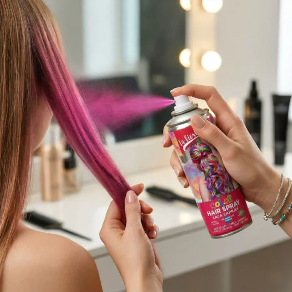 Primer plano de una mano sosteniendo la lata de spray "La Fiesta" y rociando una ráfaga de pigmento rosa vibrante sobre un mechón de cabello castaño, logrando una cobertura instantánea.