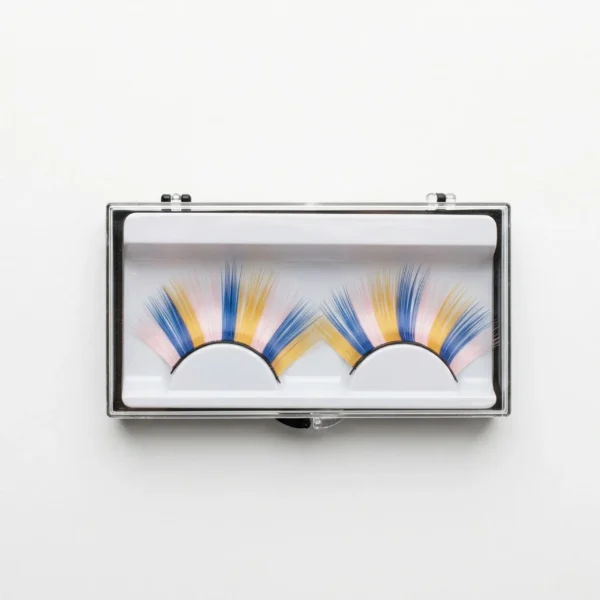 Estuche transparente con un par de pestañas postizas de colores vibrantes en tonos azul, amarillo y rosa pastel sobre fondo blanco.