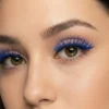 Primer plano en ángulo de tres cuartos del ojo marrón de una mujer, mostrando la longitud, volumen y textura con purpurina de las pestañas postizas azules.