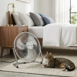 Gato descansando frente a un ventilador de suelo metálico industrial DV-TECH en un dormitorio iluminado y acogedor.