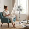 Mujer relajada leyendo en un sillón con el ventilador de pie DVTECH funcionando de forma silenciosa en la sala de estar.