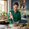Mujer preparando un smoothie de frutos rojos y espinacas con una batidora de mano ergonómica en una cocina moderna.