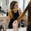 Mujer aplicando spray de color oro en las puntas del cabello frente al espejo con guantes para un retoque de color rápido.