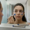 Mujer aplicando diseño artístico con barra de maquillaje azul frente al espejo para tutorial de caracterización.