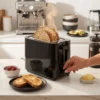 Tostadora moderna de color negro en una cocina minimalista junto a un desayuno saludable, ideal para tostar pan de pueblo y rebanadas anchas.