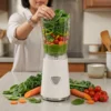 Persona preparando un batido verde detox con espinacas, brócoli y zanahoria en una licuadora individual de vaso.