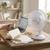 Ventilador pequeño de mesa DVTECH en un escritorio de madera junto a un ordenador y libros, ideal para estudiar o teletrabajar.