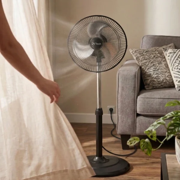 Ventilador de pie negro junto a un sofá en un salón, refrescando el ambiente con un flujo de aire potente y silencioso.