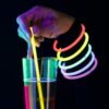 Mano sosteniendo un vaso iluminado decorado con pulseras fluorescentes Lumi Flex en una fiesta nocturna