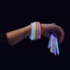 Mano mostrando pulseras luminosas GlowMaster Pro encendidas con colores intensos en ambiente oscuro