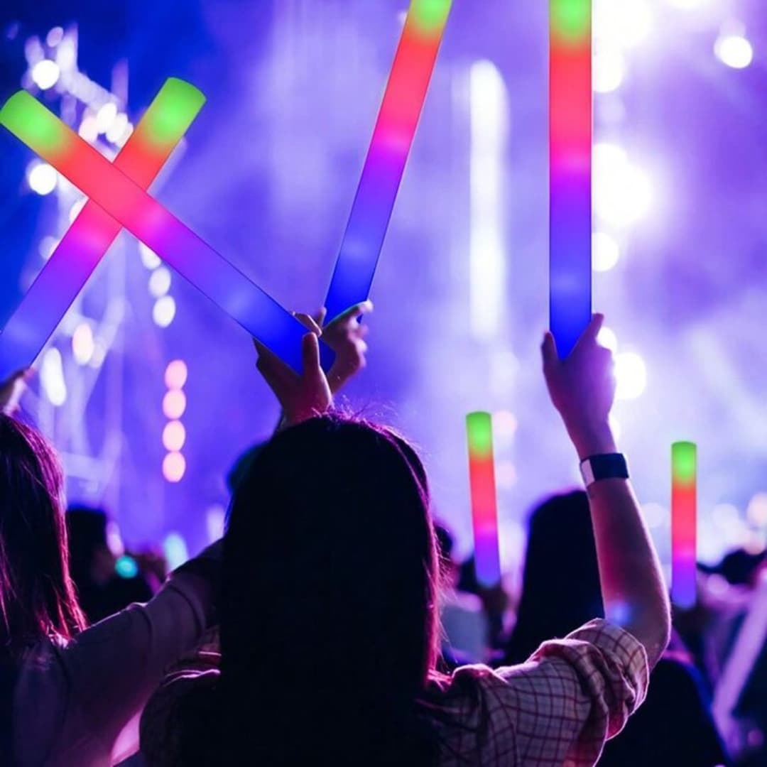 Público en un concierto nocturno agitando palos de espuma LED Foam Master 100 Ultra encendidos en varios colores