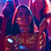 Chica en una fiesta con gel glitter UV biodegradable LumiGlow Pro aplicado en rostro y cuerpo bajo luces de neón