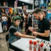 Aplicación de Sangre Artificial para Caracterización Un maquillador profesional aplicando el spray de sangre decorativa en el brazo de una mujer con caracterización de heridas realistas en un evento de disfraces