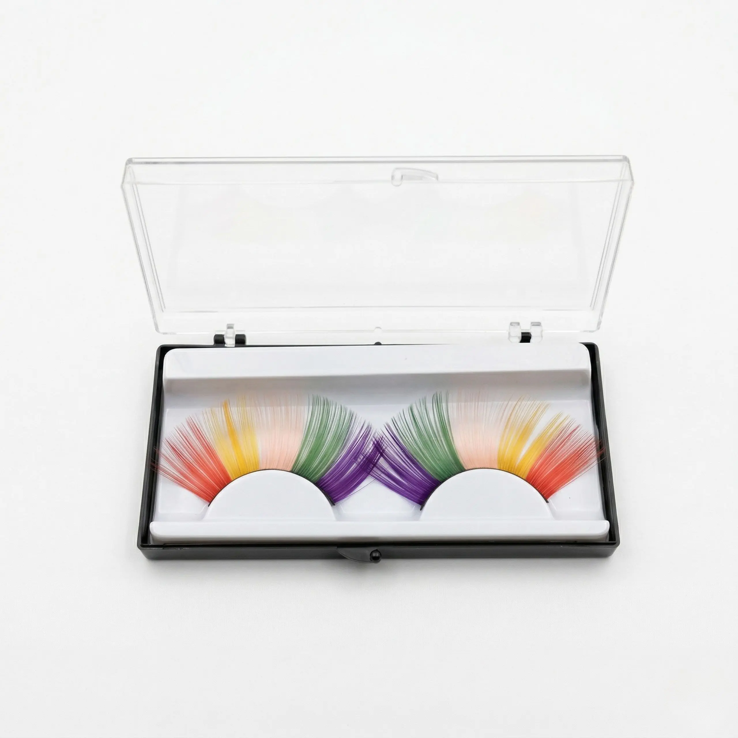 Pestañas Arcoíris en Estuche Premium Pestañas postizas arcoíris de colores vibrantes en su caja de almacenamiento transparente sobre fondo blanco profesional.