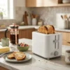 Tostadora blanca de dos ranuras extra anchas CT-818 en una cocina moderna, tostando pan artesanal para el desayuno junto a una cafetera.